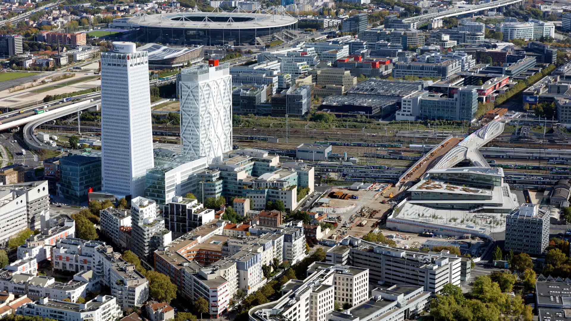 Visuel : 93 Seine-Saint-Denis Région Île-de-France / Saint-Denis : Le quartier Pleyel avec la tour Pleyel / L'autoroute A86 et le Stade de France avec le Centre Aquatique Olympique en arrière plan/ La gare du Grand Paris Express "Saint-Denis - PLeyel" (interconnexion des lignes 14, 15, 16 & 17) en premier plan et à droite de l'image - © Ph.Guignard/air-images.net, Direction de l'Observatoire Territorial / Photographe Philippe GUIGNARD (Air Images)